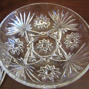 May include: A clear glass bowl with a starburst pattern. The bowl has a scalloped edge and is decorated with a repeating pattern of stars and geometric shapes.