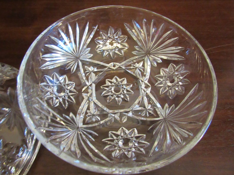 May include: A clear glass bowl with a starburst pattern. The bowl has a scalloped edge and is decorated with a repeating pattern of stars and geometric shapes.