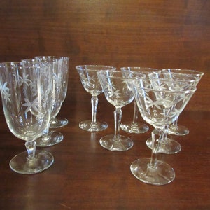 May include: Set of nine clear glass drinking glasses with etched floral designs. The glasses include six smaller glasses and three taller glasses.