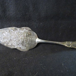 Puede incluir: Servidor de pastel de plata con un diseño floral adornado y la inscripción "Feliz cumpleaños".