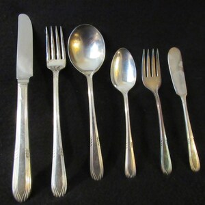 May include: A set of five silver-plated utensils, including a knife, fork, spoon, and two smaller spoons. The utensils have a simple, elegant design with a slightly curved handle.