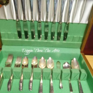 Puede incluir: Un juego de cubiertos antiguos en una caja de madera con interior verde. El juego incluye cuchillos, tenedores y cucharas, cuidadosamente dispuestos. El texto "Diggin Thru The Attic" es visible en la parte superior derecha.
