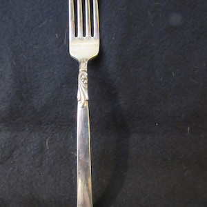 May include: A silver fork with a decorative handle. The fork has four tines and a long, slender handle.