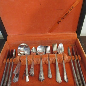 May include: A wooden box with an orange velvet lining, containing a set of silver flatware. The box is labeled "Wm. Rogers & Son".