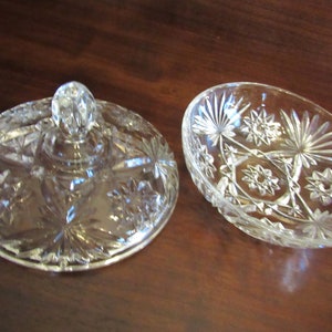 May include: A clear glass bowl with a lid, both with a cut-glass star pattern. The lid has a knob on top.