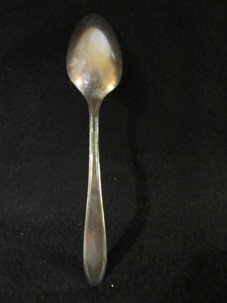 May include: A silver teaspoon with a rounded bowl and a long, slender handle.
