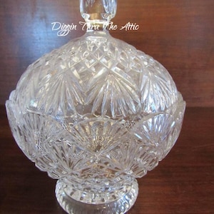 Puede incluir: Un tazón de servir de vidrio transparente con tapa. El tazón tiene un diseño de vidrio cortado y una base de pedestal. La tapa tiene un pomo en la parte superior.