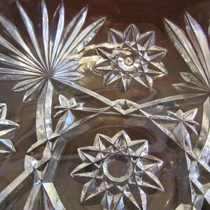 May include: Close-up of a clear glass bowl with a cut glass design. The design features a repeating pattern of stars and palm leaves.