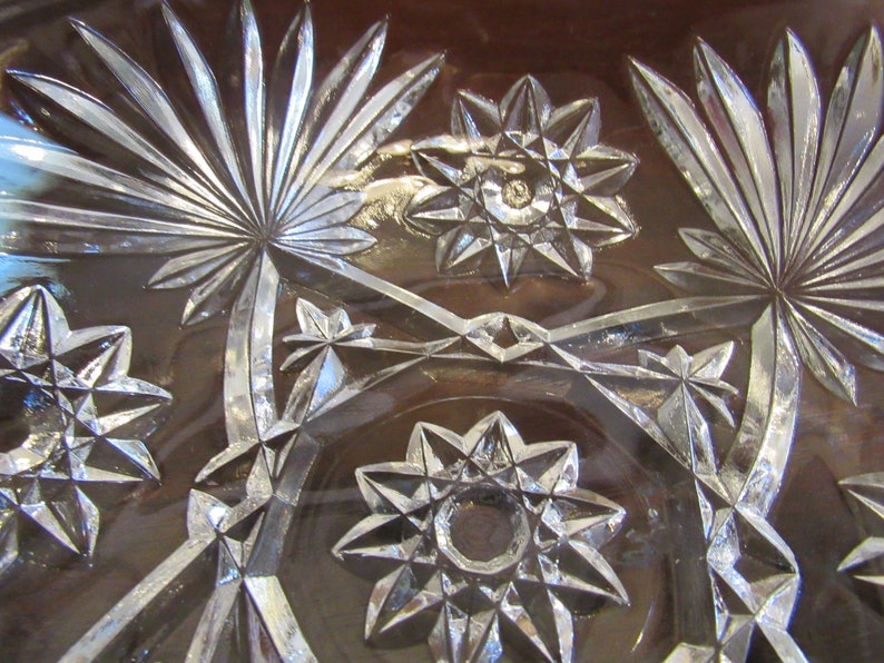 May include: Close-up of a clear glass bowl with a cut glass design. The design features a repeating pattern of stars and palm leaves.