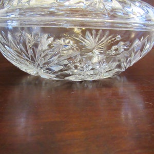 May include: A clear glass bowl with a cut glass design. The bowl is on a wooden surface.