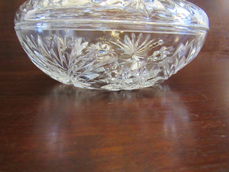 May include: A clear glass bowl with a cut glass design. The bowl is on a wooden surface.