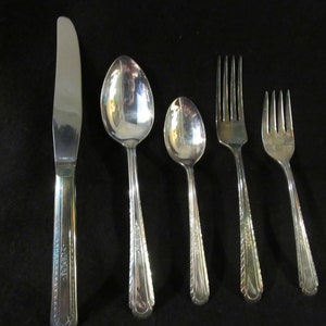 Puede incluir: Un juego de cinco cubiertos plateados, que incluye un cuchillo, dos cucharas y dos tenedores. Los cubiertos tienen un diseño adornado en los mangos.