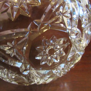 May include: A clear glass bowl with a starburst pattern. The bowl is made of cut glass and has a shiny finish.