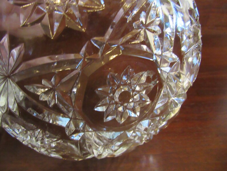 May include: A clear glass bowl with a starburst pattern. The bowl is made of cut glass and has a shiny finish.