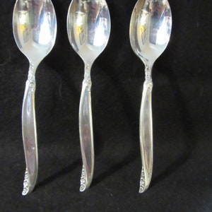 May include: Three silver spoons with ornate handles. The spoons have a polished finish and are arranged in a row.