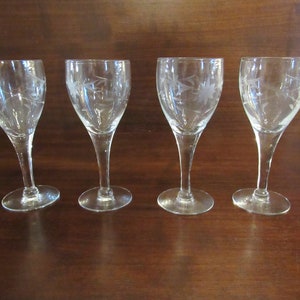 May include: Set of four clear glass wine glasses with etched floral designs. The glasses have a tall, slender stem and a round bowl.