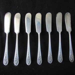 May include: Set of eight silver butter knives with ornate floral designs on the handles.