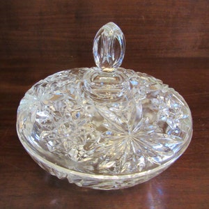 May include: A clear glass candy dish with a lid. The dish has a cut glass design with a starburst pattern. The lid has a knob on top.