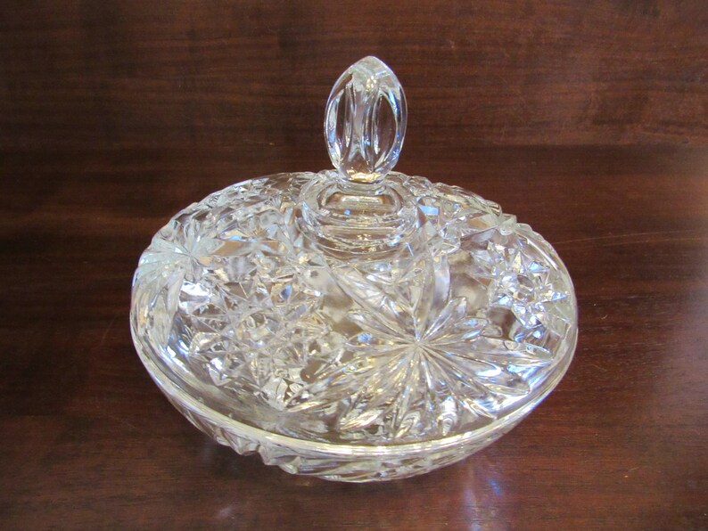 May include: A clear glass candy dish with a lid. The dish has a cut glass design with a starburst pattern. The lid has a knob on top.