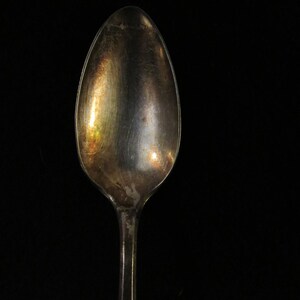 May include: A silver spoon with a tarnished finish. The spoon is oval shaped and has a long handle.