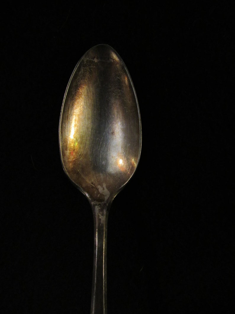 May include: A silver spoon with a tarnished finish. The spoon is oval shaped and has a long handle.