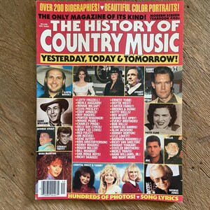 May include: A vintage magazine titled The History of Country Music, Yesterday, Today & Tomorrow. The red cover features numerous color portraits of country music artists, including Garth Brooks, Johnny Cash, and Patsy Cline, with a list of names.
