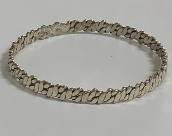 May include: A silver bangle bracelet with a braided design. The bracelet is made of a series of small, oval-shaped links that are woven together to create a textured look.