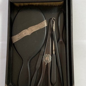 May include: A black wooden vanity set with a mirror, brush, and various tools. The set is decorated with silver accents and floral designs.