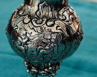 May include: A silver vase with an ornate floral design and three legs. The vase is on a blue surface.