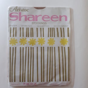 Op de afbeelding: Een wit pakket met roze en bruine tekst die "Aristoc Shaheen Stockings Sheer Stretch Seamfree Micromesh" zegt. Het pakket heeft een geel en bruin patroon met vijf gele bloemen.