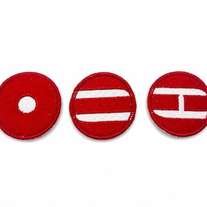 May include: Three circular embroidered patches in red with white stitching. The first patch features a central white dot, the second has two horizontal white stripes, and the third displays a white letter H shape centered on the red background.