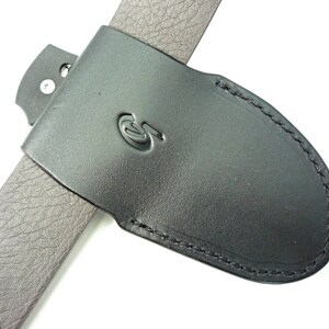 May include: Black leather belt sheath with a stitched edge and a small metal loop. The sheath has a logo on the front.