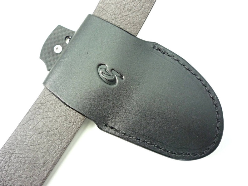 May include: Black leather belt sheath with a stitched edge and a small metal loop. The sheath has a logo on the front.