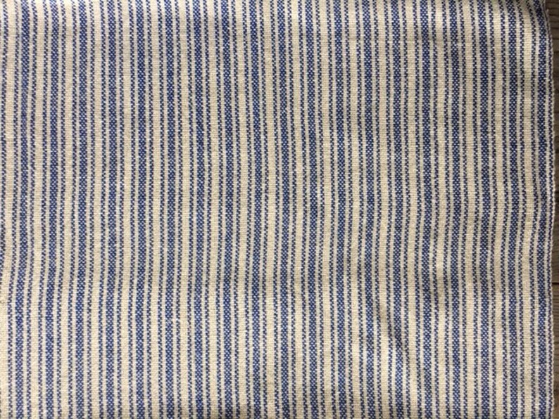 May include: A close-up of a white fabric with thin blue stripes. The fabric has a woven texture.