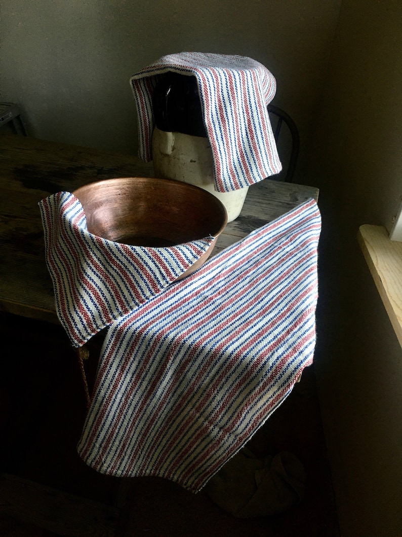May include: Two striped kitchen towels, one covering a ceramic crock and the other draped over a copper bowl. The towels are white with red and blue stripes.