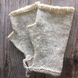 以下が含まれることがあります： 薄いグレーのニットの指なし手袋のペア。手袋は柔らかく、質感のある糸で作られており、シンプルでクラシックなデザインです。