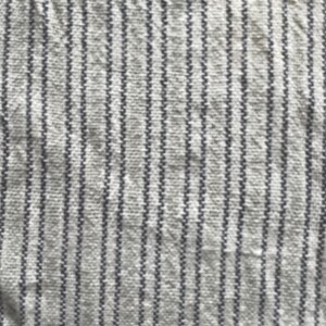 May include: Close-up of a white fabric with thin, vertical, dark gray stripes. The fabric has a textured, woven appearance.