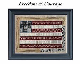 May include: A cross-stitch embroidery design featuring an American flag with the words "Freedom & Courage" stitched in red and blue thread. The design is framed in a black frame.