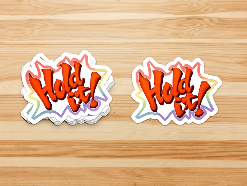 May include: A stack of "Hold It!" stickers with a rainbow border. The text is in a bold, orange font.