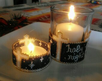 May include: Two candle holders with a black and white beaded design. The larger holder has a white candle inside and the text "Holy Night" on the front. The smaller holder has a white tea light candle inside.