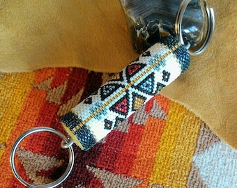 May include: A beaded key chain with a geometric pattern in black, white, red, blue, and gold. The key chain is attached to a silver key ring.