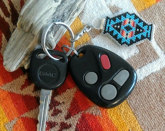 May include: A black key fob with two buttons and the text "GMC" on the key. The key fob is attached to a silver key ring with a blue and orange beaded keychain.