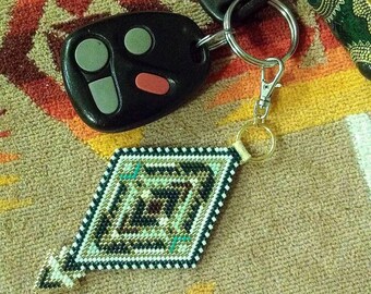 May include: A black and silver car key fob with a beaded diamond-shaped keychain. The keychain is white, black, and gold with turquoise accents.