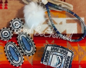 May include: A set of beaded jewelry featuring a blue and white beaded wallet, a pair of blue and white beaded earrings, and a blue and white beaded lanyard with a white pom-pom. The jewelry is displayed on a colorful patterned surface.