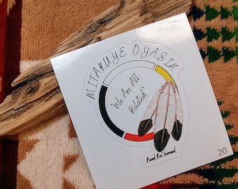 May include: White sticker with a black circle and the text "Mitakuye Oyasin" in black. Inside the circle is the text "We Are All Related" in black. The circle is divided into four sections: black, red, yellow, and white. There are two black and white feathers on the right side of the circle. The text "Bead & Chaned" is below the circle.
