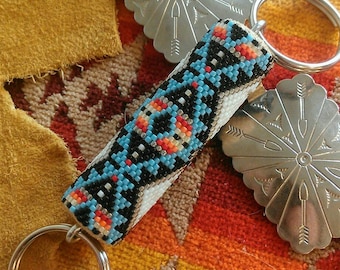 May include: A beaded keychain with a blue, black, white, red, and orange geometric pattern. The keychain is attached to a silver key ring with two silver charms.