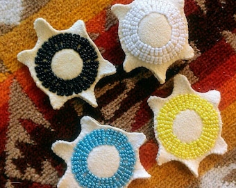 May include: Four white felt star-shaped ornaments with beaded circles in different colors: black, white, blue, and yellow.