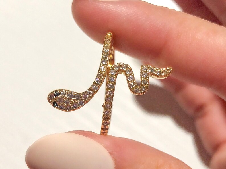 May include: A gold snake ring with clear and black stones. The snake is coiled around the ring band.