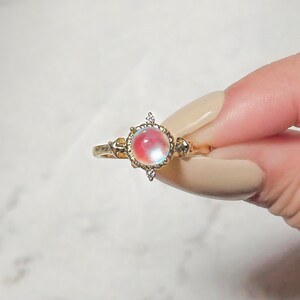 May include: A gold ring with a large iridescent gemstone surrounded by smaller clear gemstones.