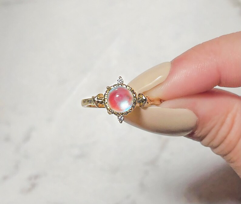 May include: A gold ring with a large iridescent gemstone surrounded by smaller clear gemstones.